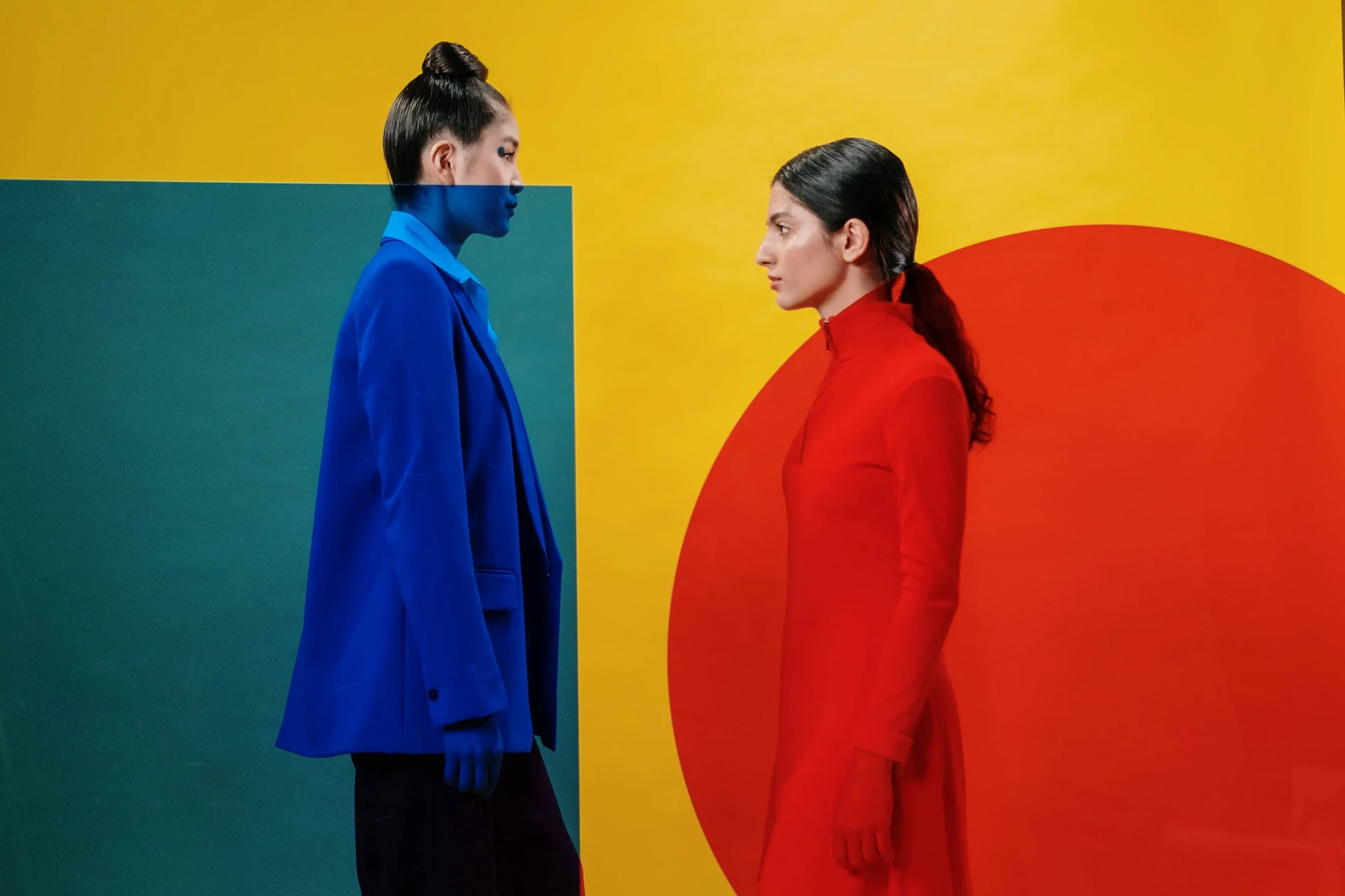 Two models in cobalt and vermilion facing each other against saturated colour fields